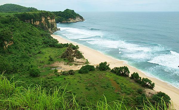 Tampak bukit hijau di depan pantai