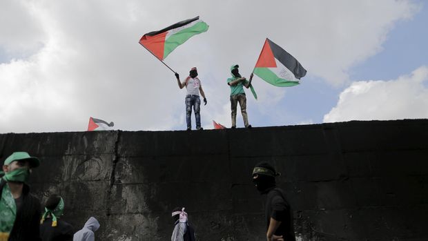 Warga Palestina mengibarkan bendera di atas tembok yang memisahkan Abu Dis, sebuah kota di Tepi Barat dengan Yerusalem.