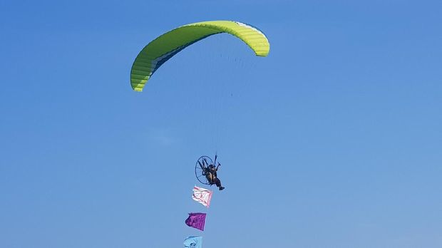 Anggota Saka Bahari dengan paramotor mengibarkan bendera pramuka di langit Pasir Putih.